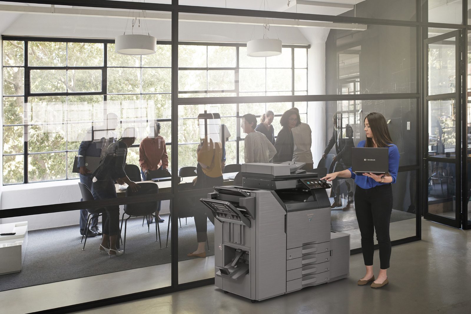 Sharp multifunction printer in a modern office setting with team meeting in background